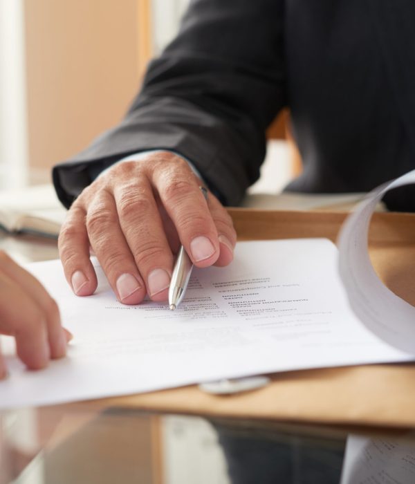 Close-up of businessman examining business contract and signing it at the office desk